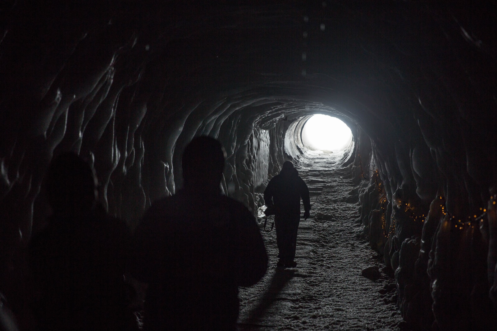 Photo by Zhifei Zhou silhouette of three person walking inside tunnel