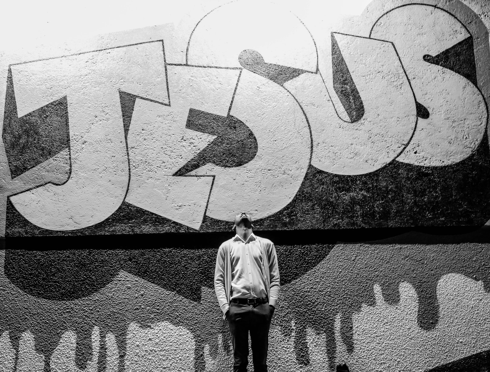 Photo by Gift Habeshaw grayscale photography of a man standing in front of a Jesus graffiti