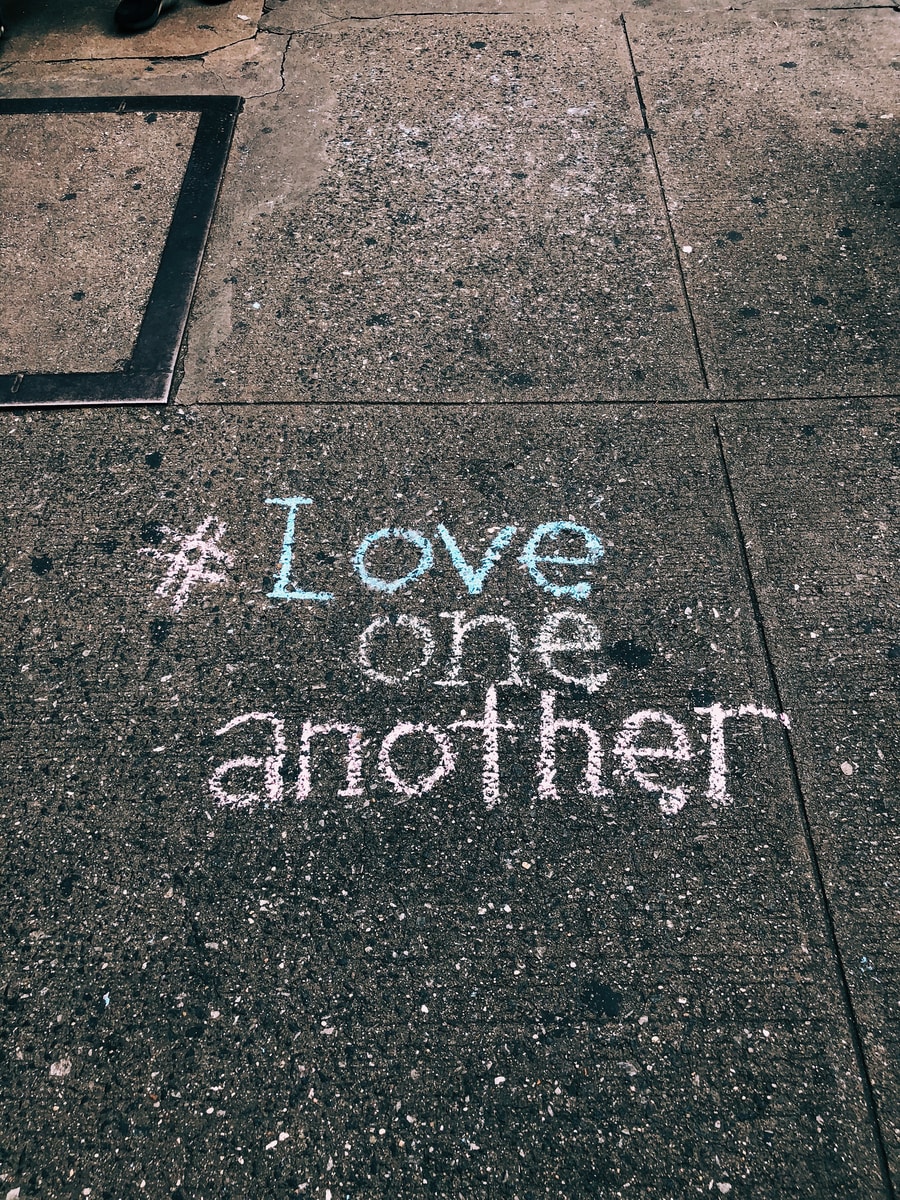 Photo by Jon Tyson love one another chalk written on concrete floor