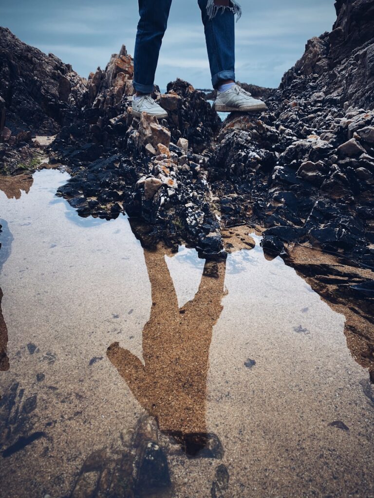 reflection of person standing on gray sand near body of water